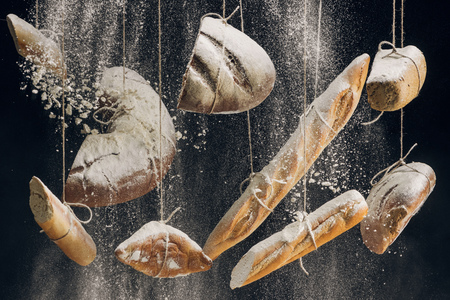 flour falling at fresh baked bread hanging on ropes on black background