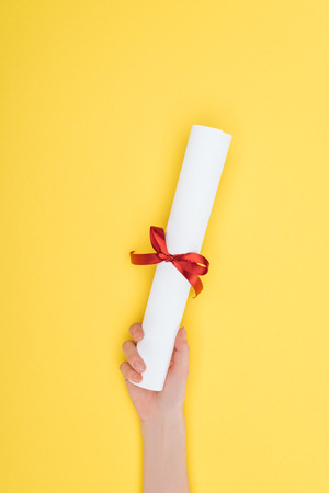 Cropped view of woman holding diploma with ribbon on yellow surfaceの写真素材