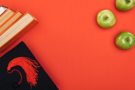 Top view of academic cap, books and apple on red surface