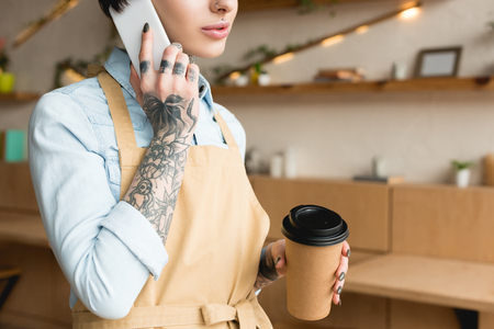 cropped view of waitress talking on smartphone and holding disposable cupの写真素材