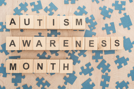 top view of autism awareness month lettering made of wooden blocks among puzzle pieces on wooden tableの写真素材