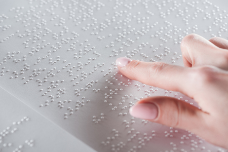 partial view of young woman reading braille text on white paperの写真素材