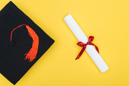 Top view of academic cap and diploma with red ribbon isolated on yellowの写真素材