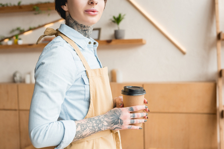 partial view of tattooed waitress in apron holding disposal cupの写真素材