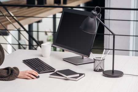 partial view of woman using computer at workplace with stationery and cupの写真素材