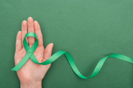 cropped view of woman holding green ribbon on green background with copy spaceの写真素材