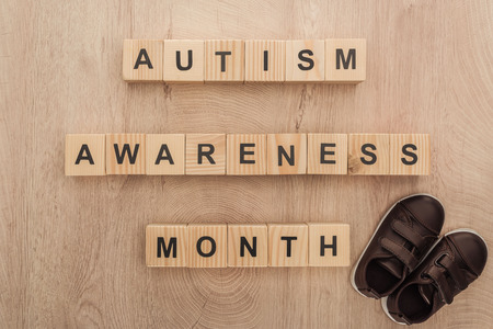 top view of autism awareness month words made of wooden blocks near brown children sneakersの写真素材