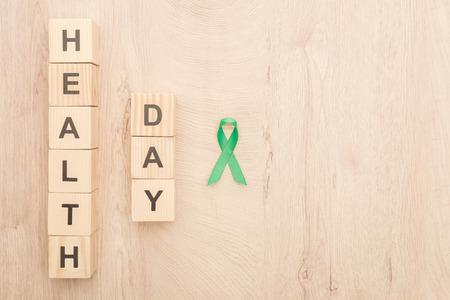 top view of cubes with health day lettering and green ribbon on wooden background