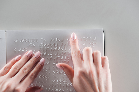 top view of young woman reading braille text on white paper isolated on greyの写真素材