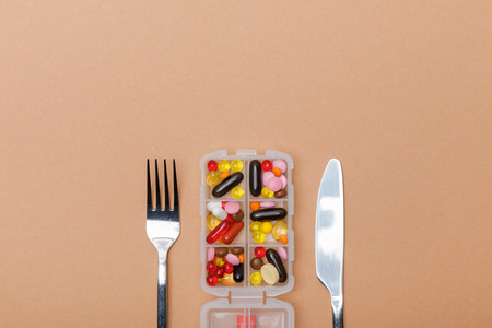 Top view of container with pills and cutlery on brown surface