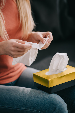 cropped view of woman holding in tissue near tissue box at homeの写真素材
