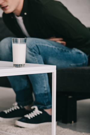 cropped view of man holding stomach and sitting near coffee table with glass of milkの写真素材