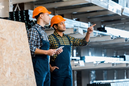 attentive indian warehouse worker pointing with hand near handsome colleagueの写真素材