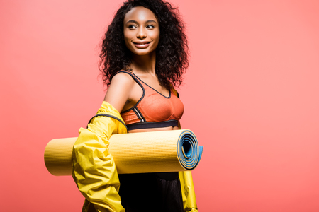 beautiful african american sportswoman holding sport mat isolated on coral with copy spaceの写真素材