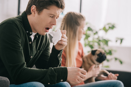 selective focus of man allergic to dog sneezing near blonde woman with pugの写真素材