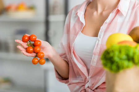 cropped view of woman holding cherry tomatoes in kitchenの写真素材