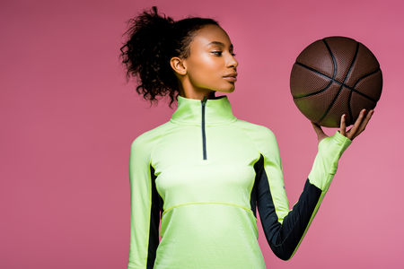beautiful african american sportswoman with basketball isolated on pinkの写真素材