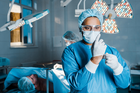 Selective focus of doctor in uniform putting off latex gloves in operating roomの写真素材