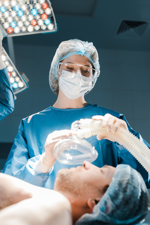 selective focus of nurse in uniform and medical cap putting mask on patientの写真素材