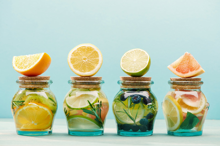 Fresh detox drinks in jars with ingredients isolated on blue background
