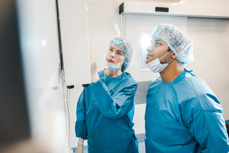 Good-looking and beautiful doctors in uniforms and medical masks looking at screenの写真素材