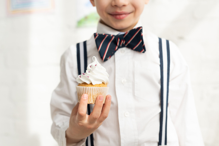 Cropped view of preteen boy in bow tie holding delicious cupcakeの写真素材