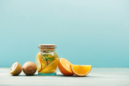 Organic fruit detox drink in jar with rosemary near oranges and kiwi isolated on blue backgroundの写真素材