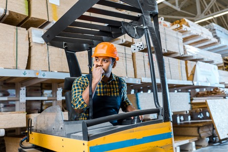 indian warehouse worker talking on walkie talkie while sitting in forklift machineの写真素材