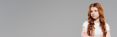 panoramic shot of upset redhead girl looking away isolated on grey with copy space