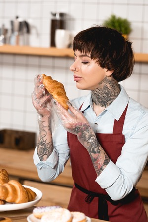 pretty barista in disposable gloves holding delicious croissantの写真素材