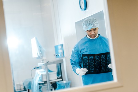 handsome doctor in uniform and medical cap holding x-ray in clinicの写真素材