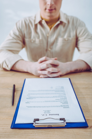 Selective focus of clipboard with resume cv lettering near pen and man with clenched handsの写真素材