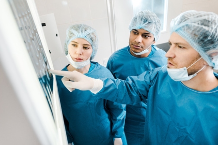 Handsome and beautiful doctors in uniforms and medical masks pointing with finger at x-rayの写真素材