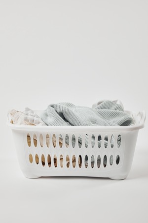 White plastic laundry basket with dirty clothes on grey backgroundの写真素材