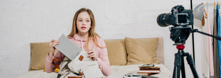 Panoramic shot of teenager holding book and backpack in front of video camera in bedroomの写真素材