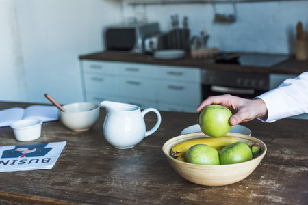 Partial view of man taking apple from bowl on wooden kitchen tableの写真素材