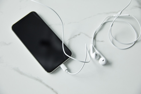 Top view of smartphone with blank screen and wired earphones on white marble surfaceの写真素材