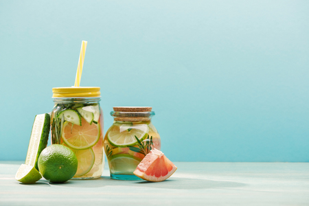 Fresh detox drinks in jars near limes, cucumber and grapefruit isolated on blue backgroundの写真素材