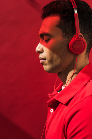 Side view of handsome mixed race man in headphones with eyes closed on red with copy spaceの写真素材