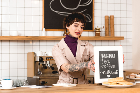smiling businesswoman placing menu board on bar counter in coffee shopの写真素材