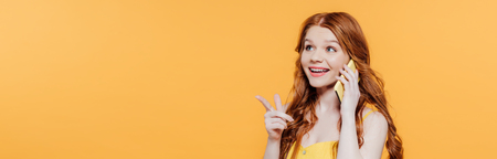 Panoramic shot of beautiful smiling redhead girl pointing with finger while talking on smartphoneの写真素材