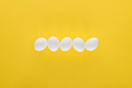 Five white chicken eggs in row on yellow backgroundの写真素材
