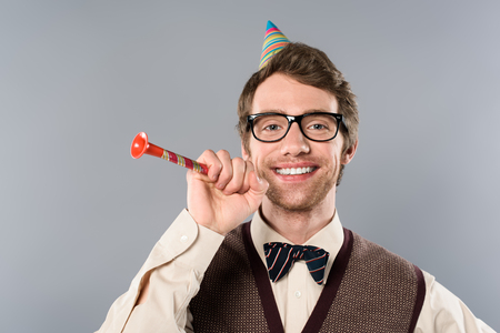 happy man in glasses and party cap holding party horn isolated on greyの写真素材