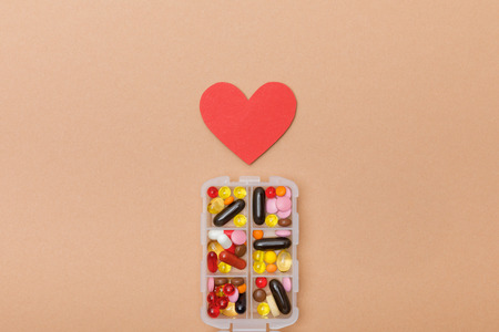 Top view of container with pills and paper heart on brown surfaceの写真素材