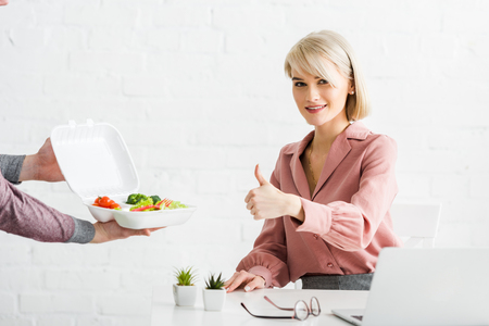 Cropped view of man holding takeaway box with vegetables near happy blonde girl showing thumb upの写真素材