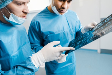 Selective focus of doctors in uniforms and medical masks pointing with finger at x-ray