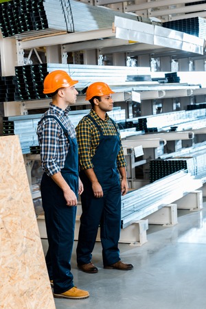 Two serious multicultural friends in uniform standing in warehouse