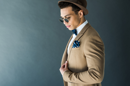 Stylish mixed race man in suit and sunglasses posing isolated on grey with copy spaceの写真素材