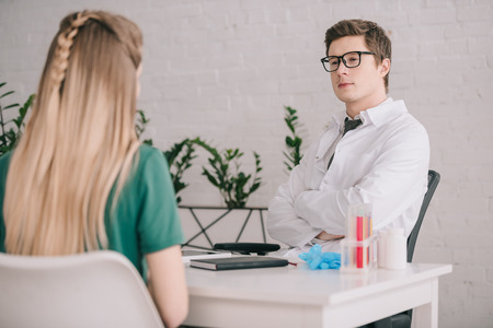 Back view of woman sitting near doctor in glasses and white coat with crossed armsの写真素材