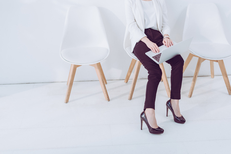 Cropped view of woman sitting on chair and using laptopの写真素材
